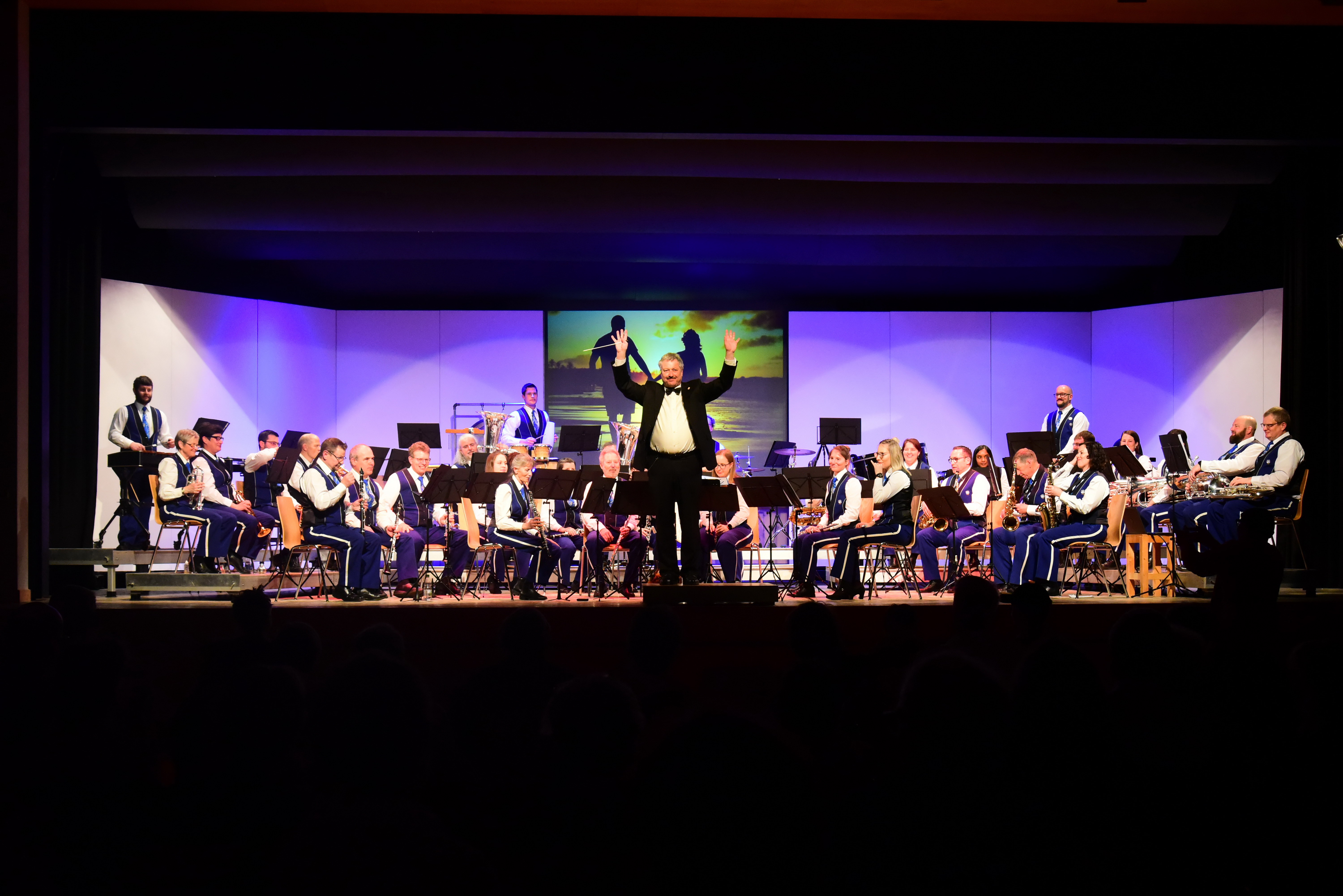 Die Harmoniemusik Schwanden sitzt auf der Bühne und der Dirigent winkt ins Publikum.